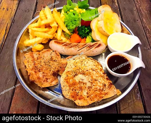 Steak mixed with gravy sauce, there are grilled Chicken, Pork chop with black pepper, grilled Sausage, French fries and Salad with cream sauce