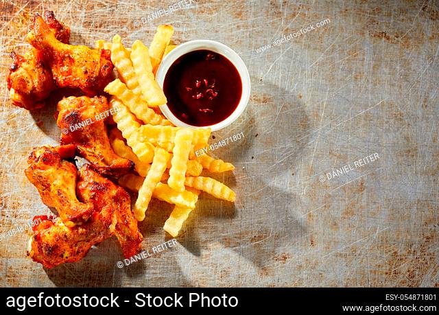 Crispy grilled hot chili pepper chicken wings with oven baked crinkle cut potato chips served with a piquant dip on an old metal background viewed top down