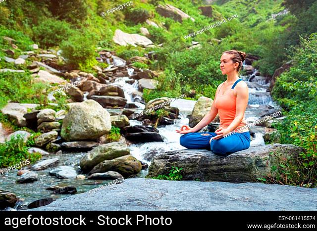 Woman doing yoga meditation asana Padmasana lotus pose outdoors at tropical waterfall