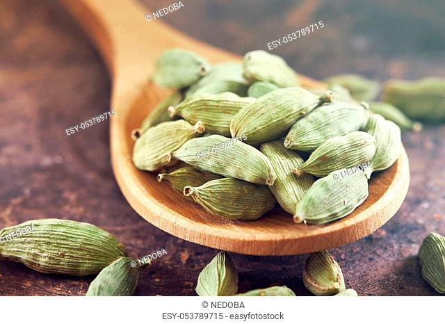 Raw green cardamom pods in wooden spoon on rustic background