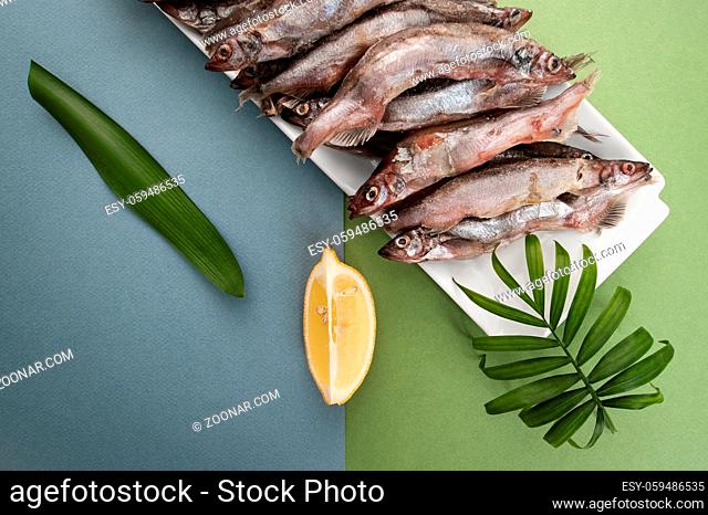Raw fresh-frozen capelin, served with lemon on a light blue-green background