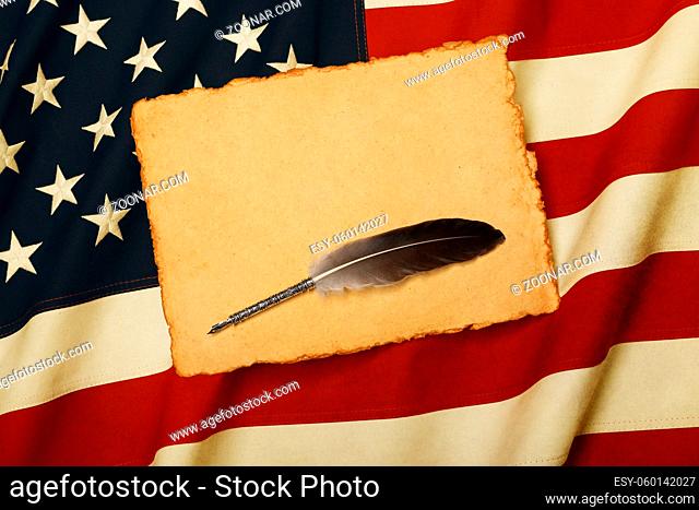 Close up blank vintage yellow paper sheet and quill on old weathered cotton embroidered US national flag background, symbol of American history