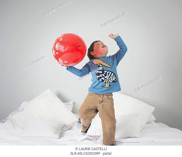 Boy playing with balloon on bed