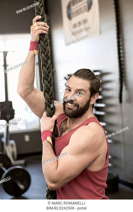 Mixed Race man climbing rope gymnasium