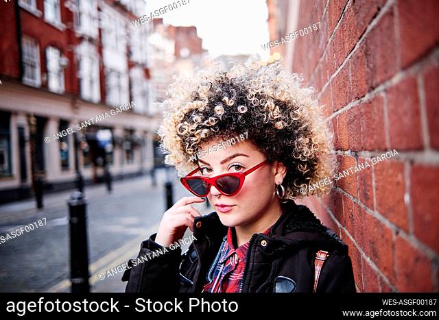 Curly haired woman wearing sunglasses by wall at Chinatown during vacations