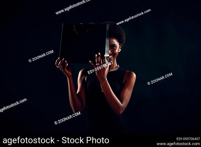 African american woman with afro hairstyle smiles and holds black shopping bags. Sale and discounts on market and Black Friday concept