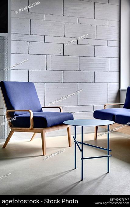 Blue armchair and a sofa with wooden legs on the background of the gray brick wall in the relax zone of the loft style office