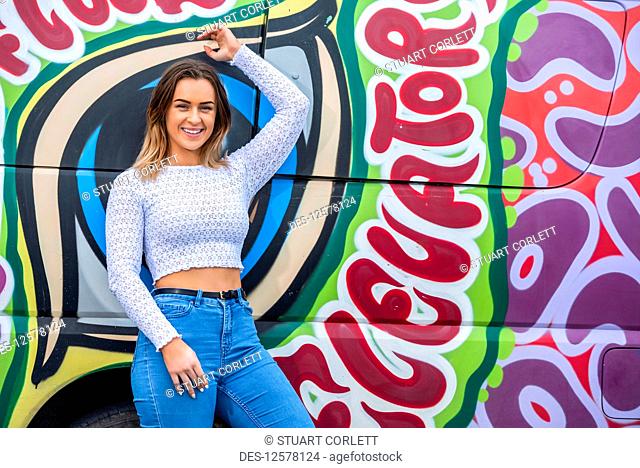 Portrait of a young woman standing against a wall of colourful street art; Wellington, North Island, New Zealand