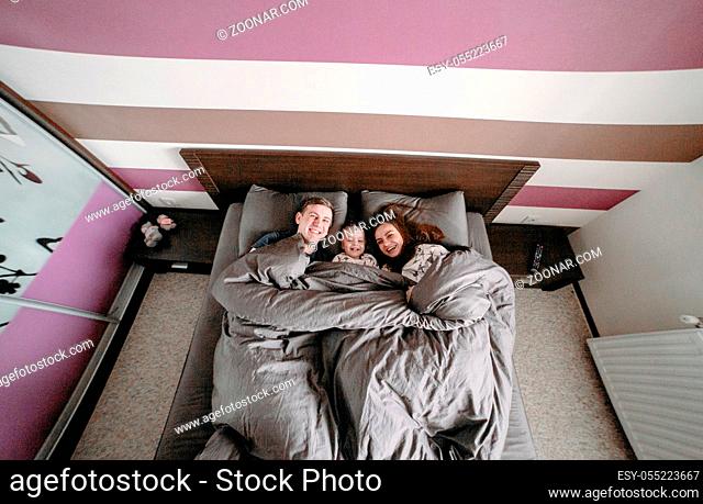 Dad, mom and little daughter together in bed in the bedroom