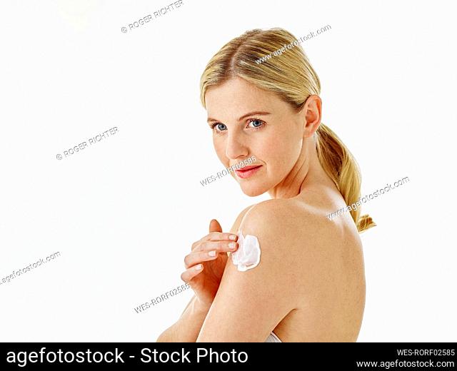 Young woman applying cream on hand while standing against white background