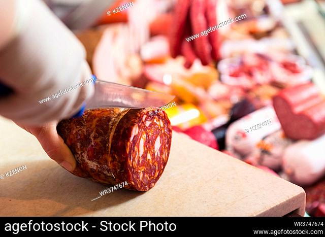 Butcher woman cutting chorizo sausage on board