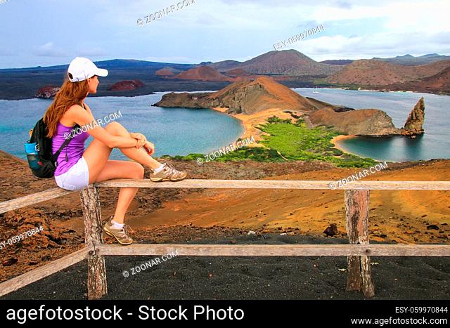 Young woman enjoying the view of Pinnacle Rock on Bartolome island, Galapagos National Park, Ecuador. This island offers some of the most beautiful landscapes...