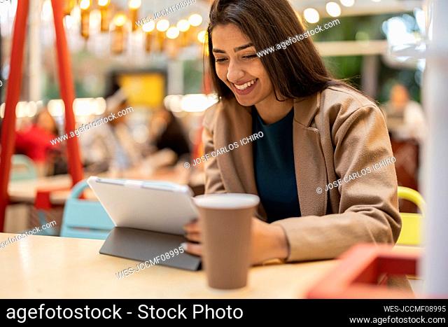 Happy woman using tablet PC sitting in cafe
