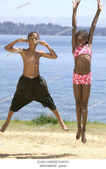 Young African-American boy and girl jump in park by lake