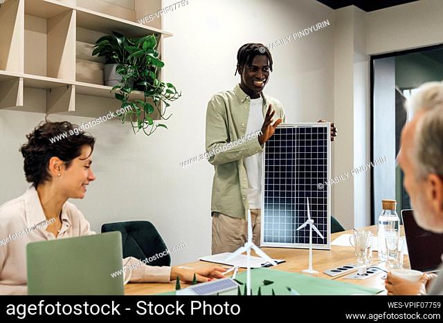 Young businessman discussing over solar panel with colleagues in office