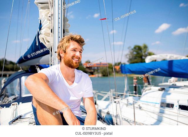 Young man sitting on sailboat on Chiemsee lakeside, Bavaria, Germany
