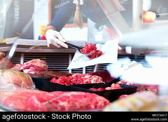 Meat in a butcher shop display being put in by sales woman, close-up