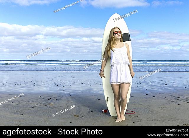 Female wearing sunglasses standing at the beach with surfboard. Horizontal outdoors shot