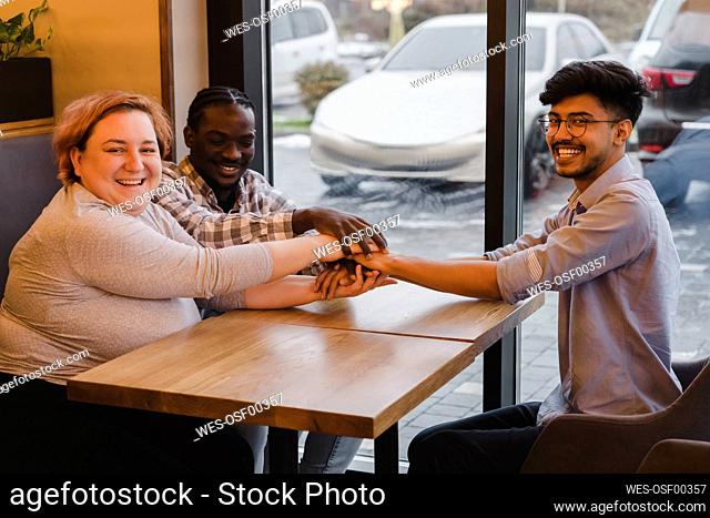 Happy multiracial friends stacking hands at table in cafe