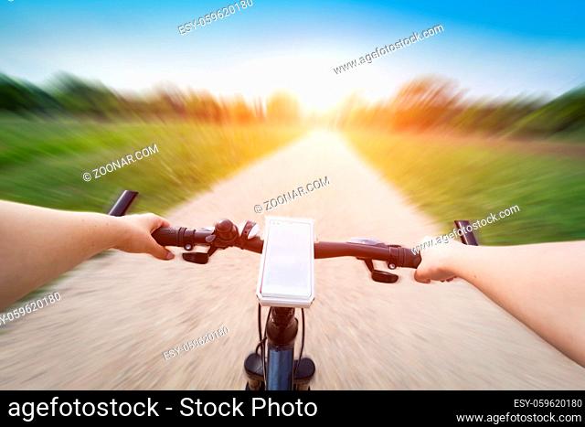 Riding a bike first person perspective. Smartphone attached to handlebar. Speed motion blur. Countryside road towards sun