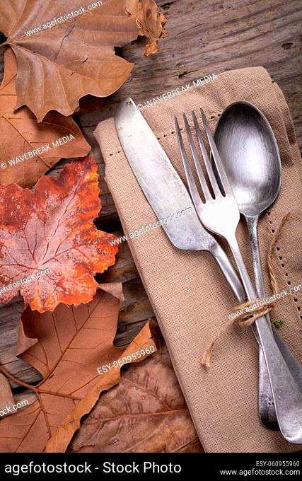 Close up of multiple autumn leaves and cutlery set over a napkin on wooden surface