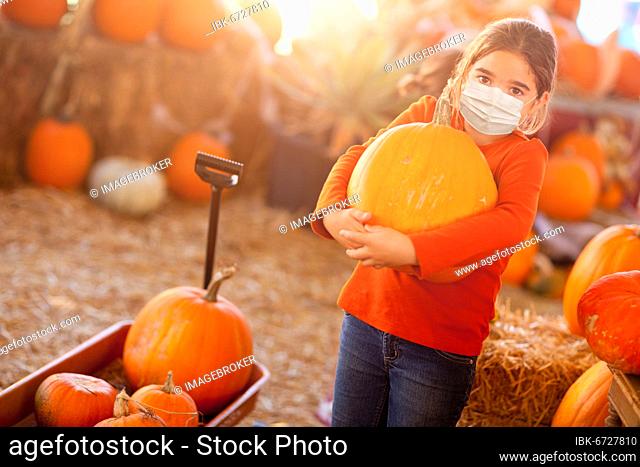 Cute girl choosing A pumpkin at pumpkin patch wearing medical face mask