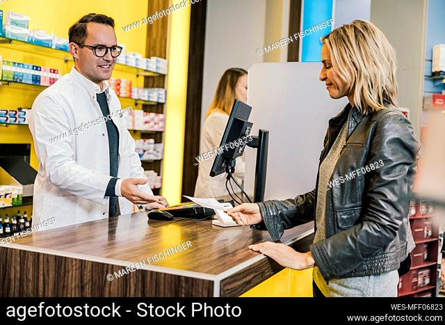 Smiling customer giving prescription to salesman in chemist store