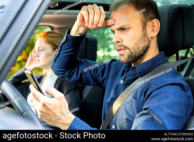 Frustrated young man using smart phone while driving a car