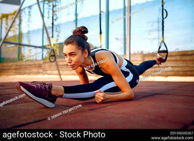 Woman sits on the splits on sports ground outdoors. Slim female person in sportswear, outside fitness training, fit workout