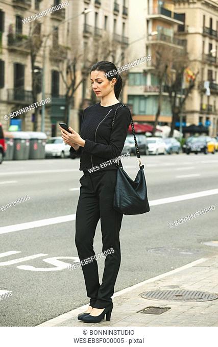 Spain, Catalunya, Barcelona, young black dressed businesswoman telephoning in front of a street