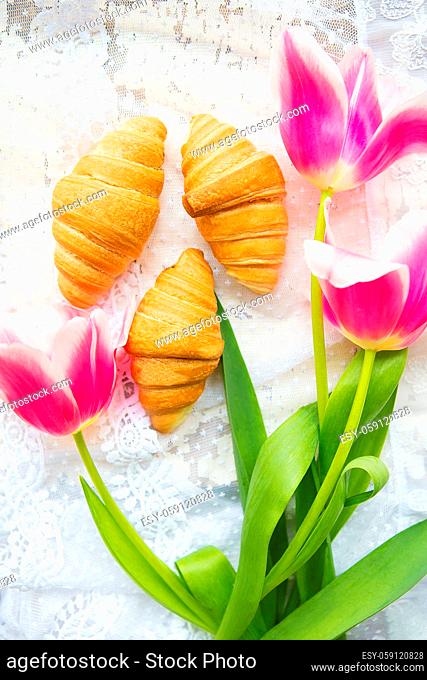 Three croissants and bright pink tulips on lace tablecloth