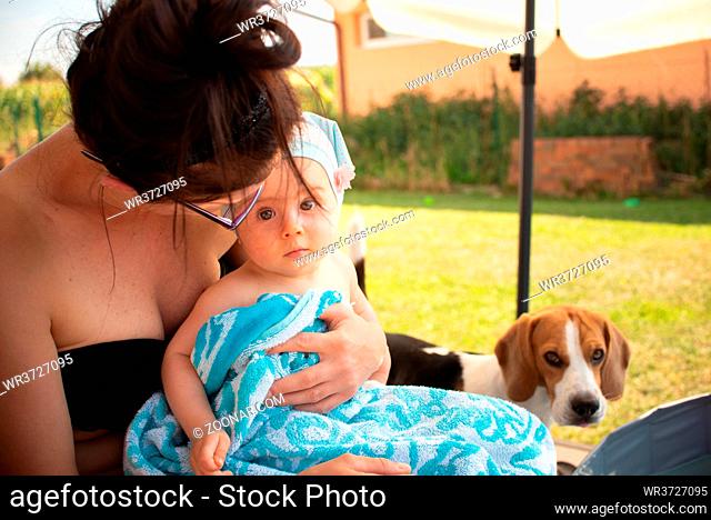 Mother holding baby girl on lap, covered with towel after swimming. Summer activities