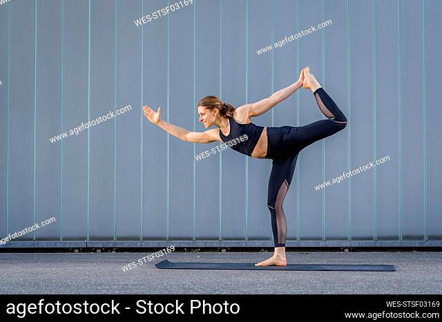 Smiling woman standing on one leg practicing yoga in front of wall