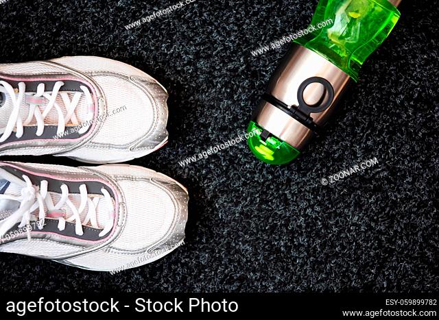 Running shoes and bottle of water on a dark background