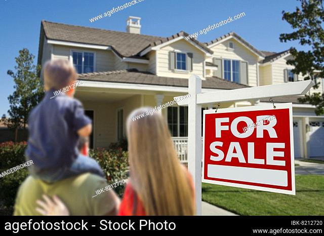 Young family looking at a beautiful new home with a for sale real estate sign in front