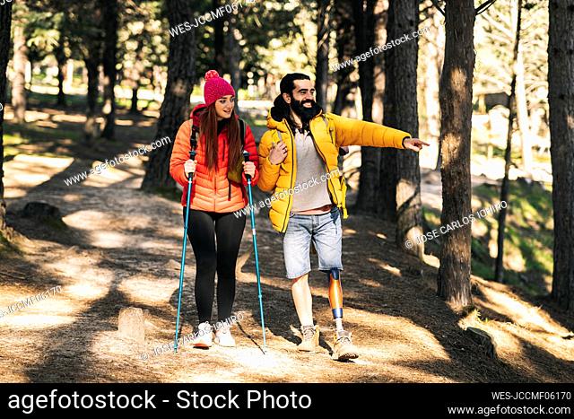 Happy disabled man pointing away by woman walking with hiking pole in forest