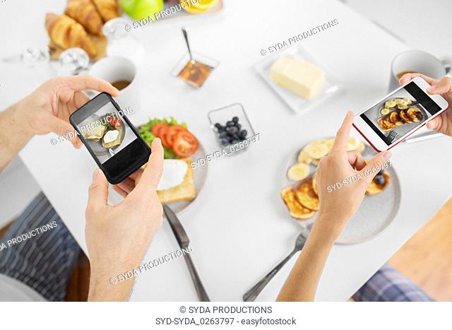 close up of couple with smartphones at breakfast
