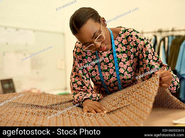Young African female fashion designer examining some material while working at a bench in her manufacturing studio
