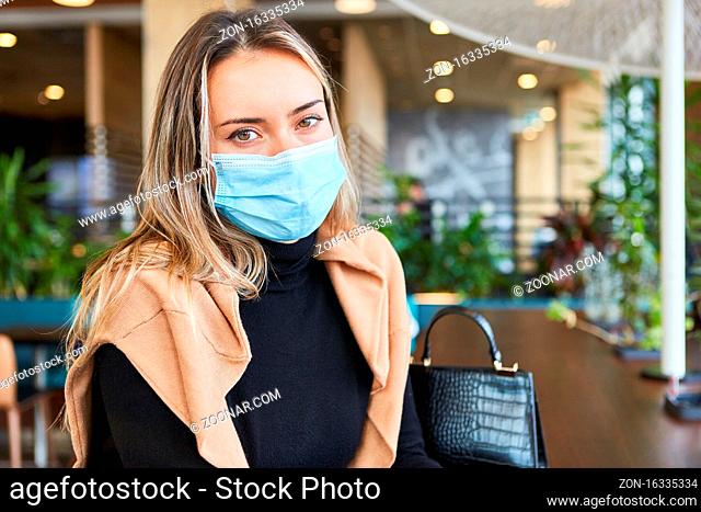 Frau mit Gesichtsmaske wegen Covid-19 Pandemie sitzt in einem Cafe oder Restaurant