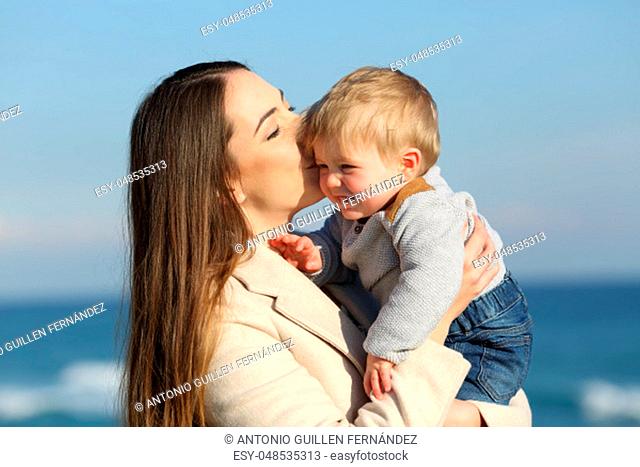 Happy mother kissing her kid son outdoors on the beach