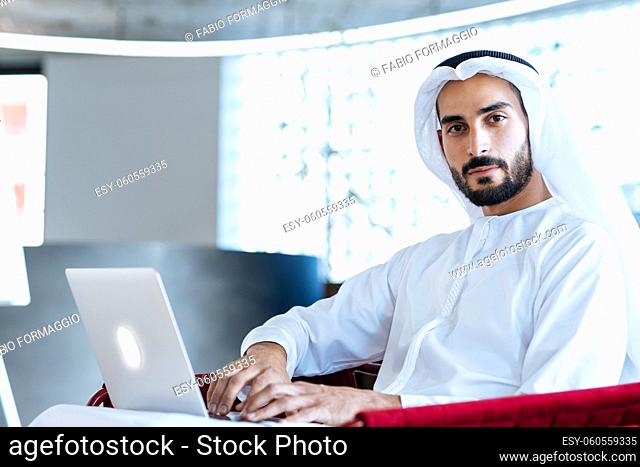 handsome man with dish dasha working in his business office of Dubai. Portraits of a successful businessman in traditional emirates white dress