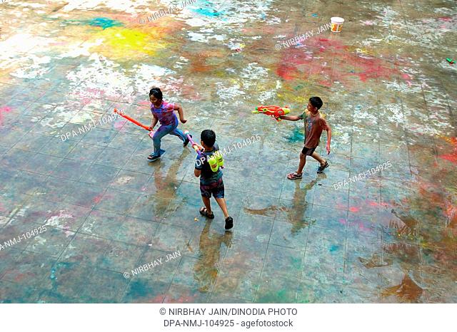 Three children playing Holi festival of color at Ananta apartments at Breach Candy  ; Bombay Mumbai  ; Maharashtra  ; India
