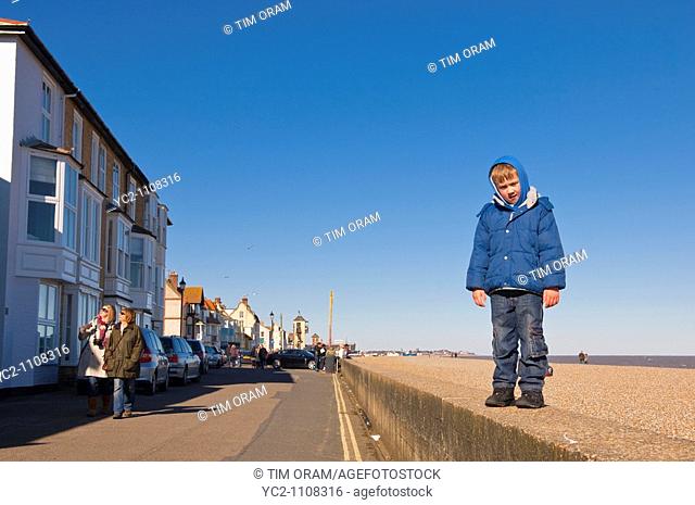 A picture of a 6 year old boy standing on the sea wall at Aldeburgh , Suffolk , England , Britain , Uk