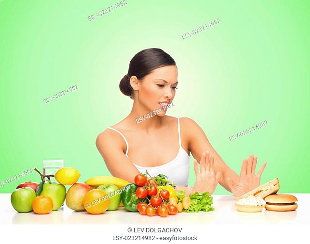 people, junk food, healthy eating, diet and weight loss concept - woman with fruits and vegetables rejecting hamburger over green background