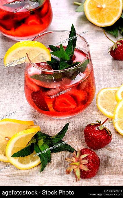 A glass of chilled strawberry lemonade, mint leaves, a slice of lemon with ice