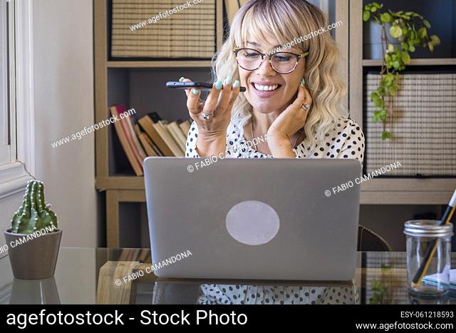 Businesswoman using laptop while talking on mobile phone in office. Busy woman at work. Woman speaking on mobile phone at office through voice call
