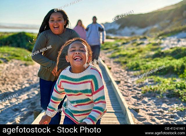 Portrait carefree sisters running on sunny beach boardwalk