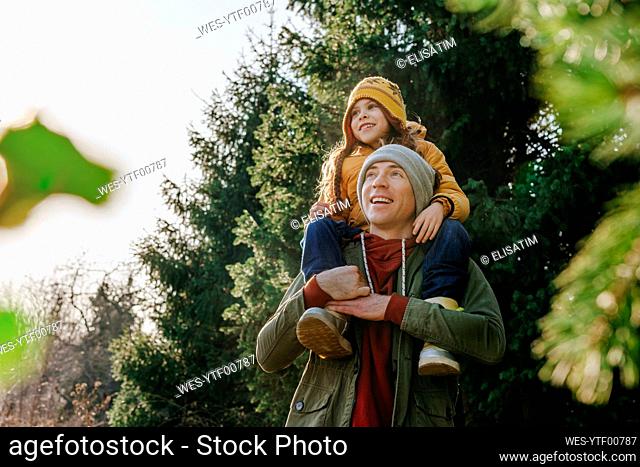 Smiling father carrying daughter on shoulders in forest