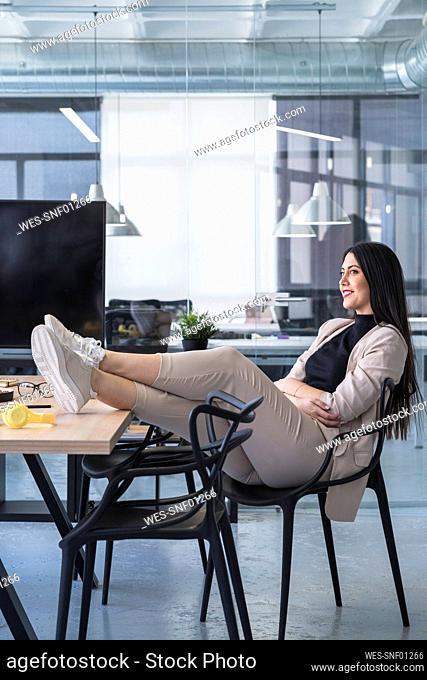 Smiling businesswoman with feet up looking away while sitting at desk in coworking office