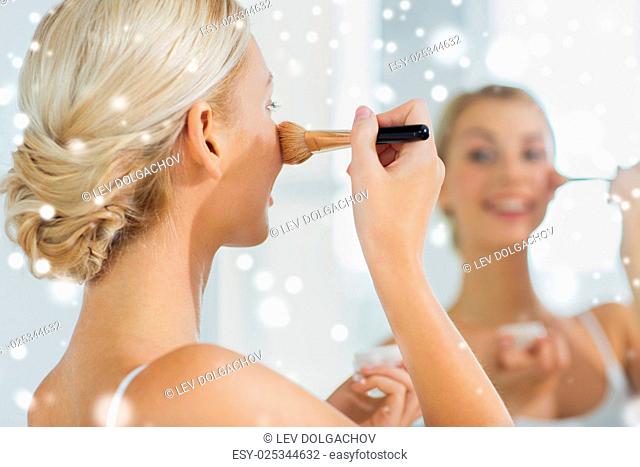beauty, make up, cosmetics, morning and people concept - close up of smiling young woman makeup brush and powder foundation looking to mirror at home bathroom...